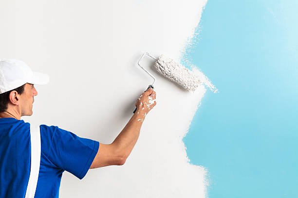 Back view of painter painting a wall with paint roller, with copy space